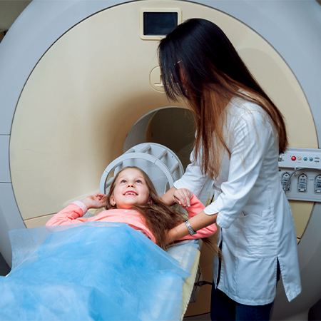 A pediatric patient smiling up at a MR personnel as the patient is being prepared for a brain scan.