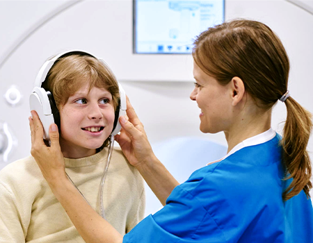 An MR personnel is preparing an older pediatric patient with hearing protection/audio headsets.