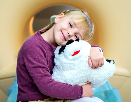 A young female MRI pediatric patient smiling and hugging a large black and white stuff animal.