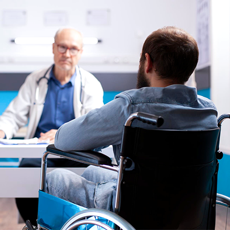 The backside of a male wheelchair user facing an older male medical personnel.