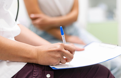 A figure filling out a paper form with another figure blurred in the background.
