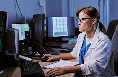 An MR personnel working on a monitor during  a scan. Blurred monitor in the background.