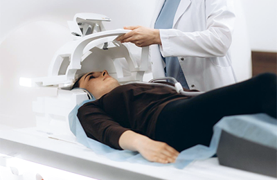 A patient is laying calmly on a scan table while an MR personnel is positioning head coil in place.