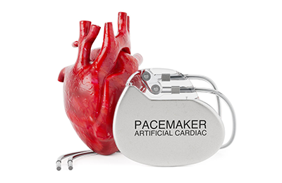 A model of a red human heart with a pacemaker with leads sitting next to it.