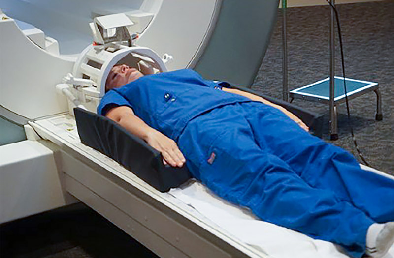 A patient with a head coil and dark blue scrubs is laying on the scan table.